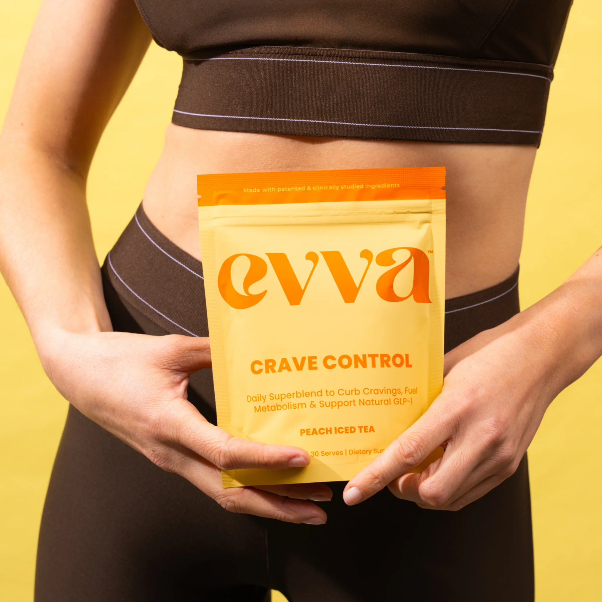 12 Person facing away with a black sports top; an orange Crave Control supplement pouch is taped to their lower back against a yellow background.