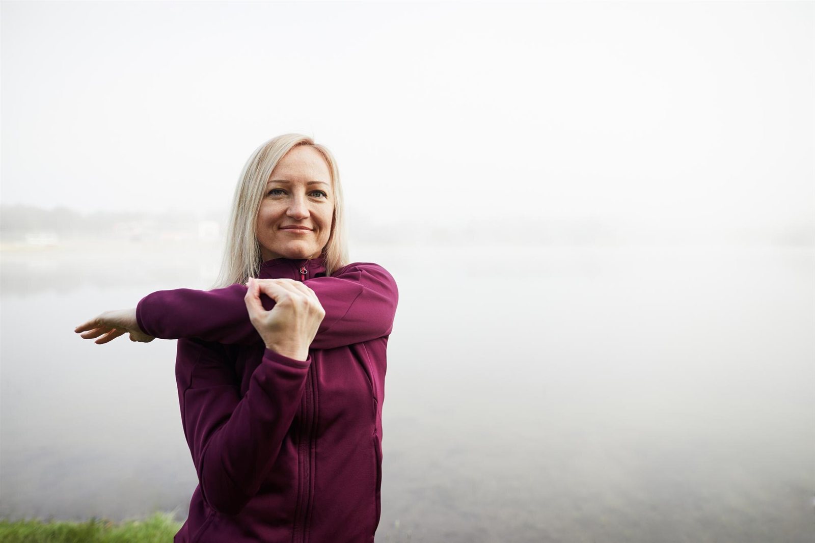 Woman stretching by a misty lake in the morning